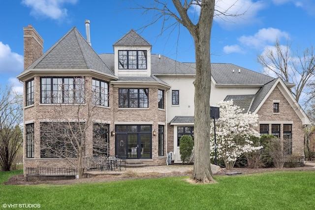 rear view of property featuring a lawn, a chimney, french doors, and brick siding