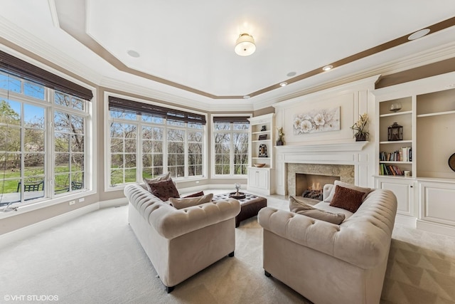 carpeted living room featuring built in features, ornamental molding, a high end fireplace, baseboards, and a tray ceiling