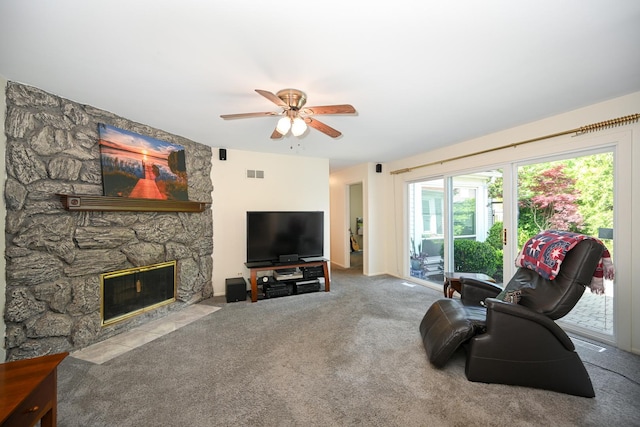 carpeted living area with a ceiling fan and a stone fireplace