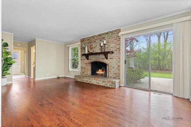 unfurnished living room featuring visible vents, a brick fireplace, wood finished floors, baseboards, and ornamental molding
