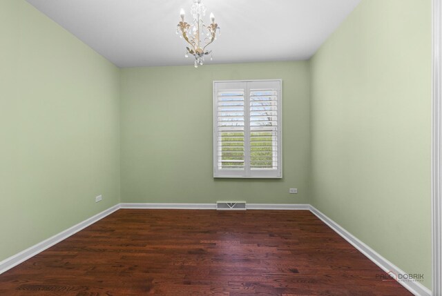 spare room featuring baseboards, dark wood finished floors, an inviting chandelier, and visible vents