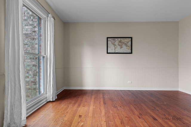 empty room with a wainscoted wall, wood finished floors, and baseboards