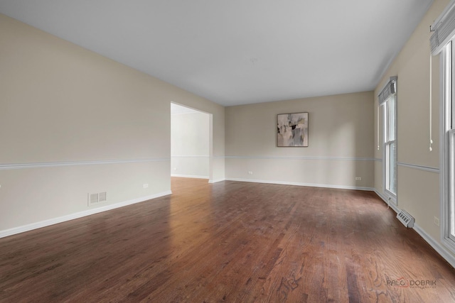 unfurnished room with baseboards, visible vents, and dark wood-type flooring