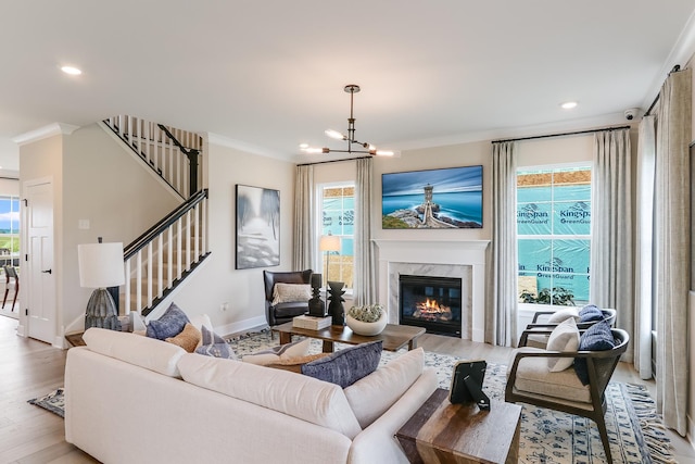 living area featuring light wood finished floors, a fireplace, stairs, and crown molding