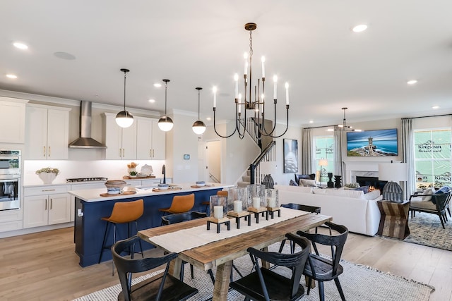 dining area featuring light wood finished floors, recessed lighting, a chandelier, crown molding, and a high end fireplace