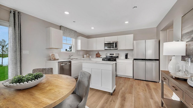 kitchen featuring light wood-style floors, appliances with stainless steel finishes, a kitchen island, a sink, and white cabinetry
