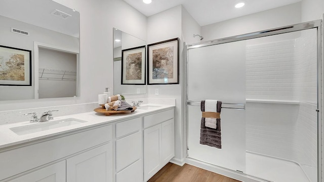 bathroom with a sink, a shower stall, double vanity, visible vents, and wood finished floors