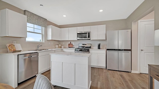 kitchen with white cabinets, a sink, appliances with stainless steel finishes, light countertops, and light wood finished floors