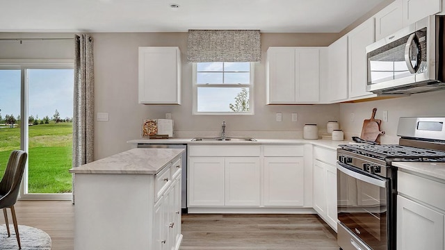 kitchen featuring white cabinetry, a sink, stainless steel appliances, a kitchen island, and light wood finished floors