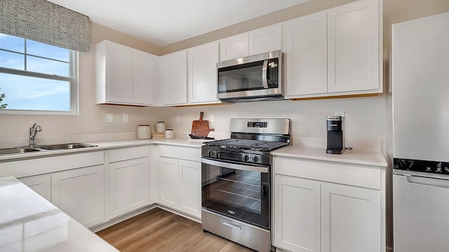 kitchen with a sink, stainless steel appliances, light wood-style floors, light countertops, and white cabinets