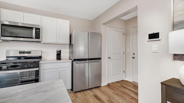 kitchen with light stone counters, light wood-style floors, stainless steel appliances, and white cabinets