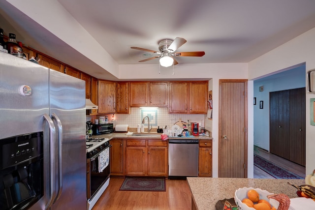 kitchen featuring brown cabinetry, light countertops, a sink, light wood finished floors, and appliances with stainless steel finishes