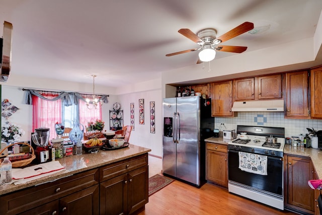kitchen featuring stainless steel fridge, light wood-style floors, backsplash, under cabinet range hood, and range with gas cooktop