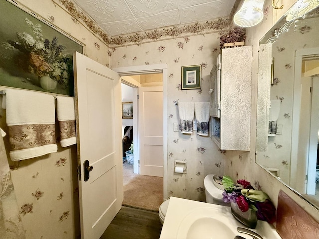 bathroom with wallpapered walls, wood finished floors, toilet, and an ornate ceiling