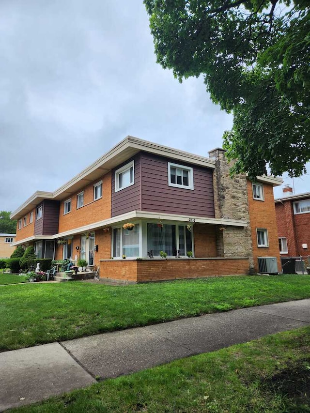 view of property with brick siding, a front lawn, and central air condition unit