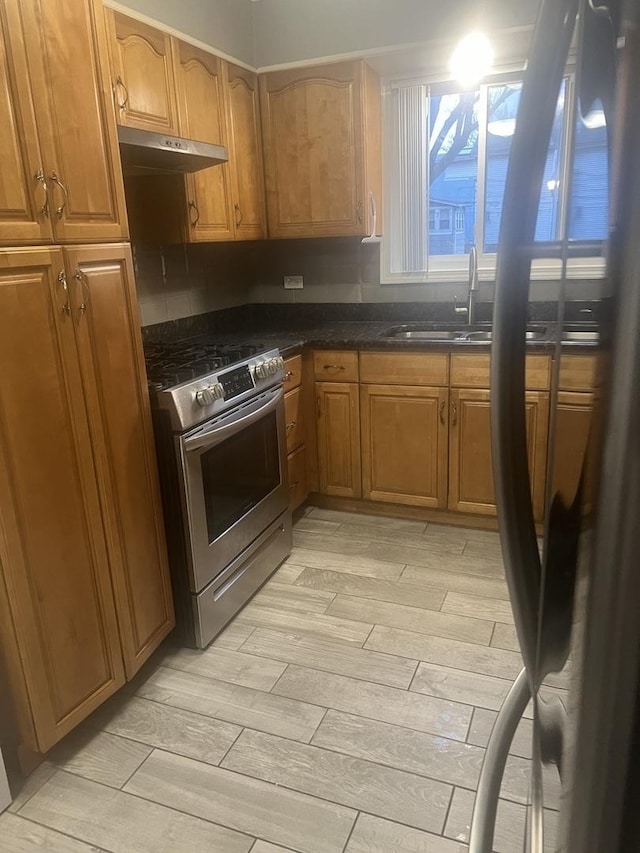 kitchen with stainless steel stove, wood finish floors, under cabinet range hood, brown cabinets, and a sink