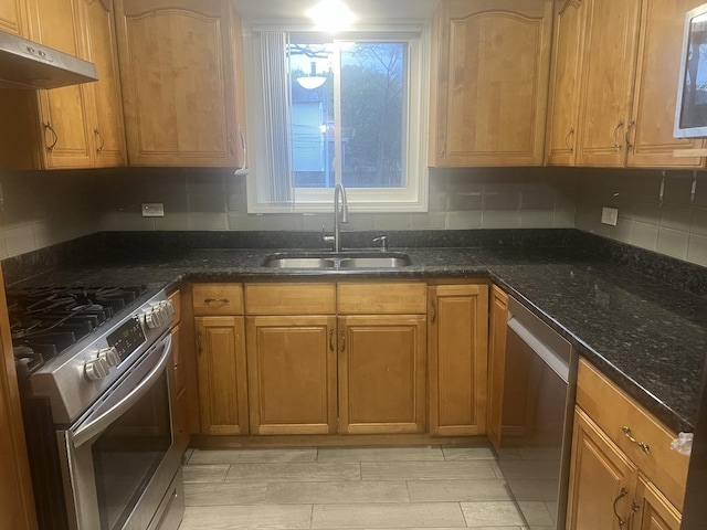 kitchen featuring decorative backsplash, appliances with stainless steel finishes, a sink, dark stone countertops, and under cabinet range hood