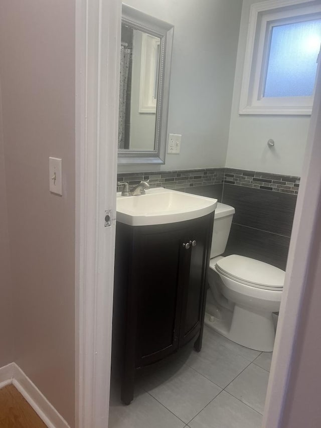 bathroom with tile patterned flooring, vanity, toilet, a wainscoted wall, and tile walls