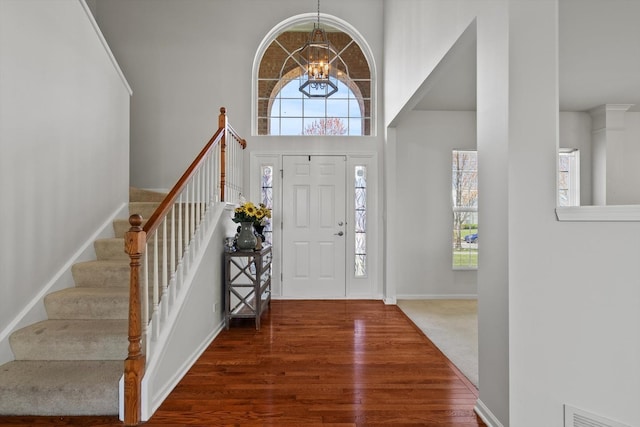 entrance foyer featuring visible vents, an inviting chandelier, a towering ceiling, wood finished floors, and stairs