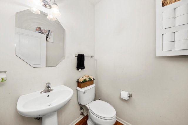 half bathroom with baseboards, toilet, and a sink