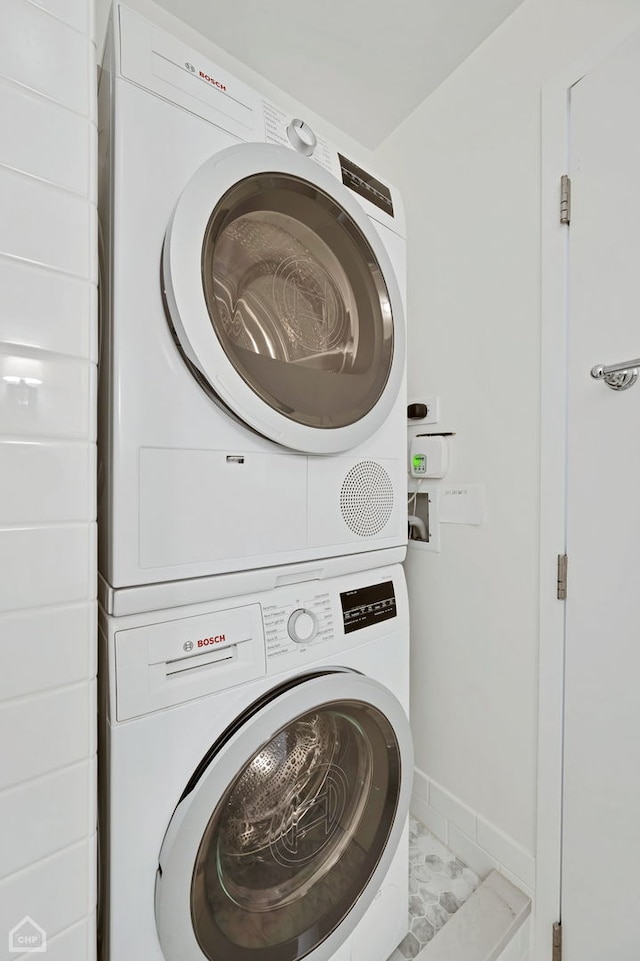 washroom featuring laundry area, baseboards, stacked washing maching and dryer, and tile patterned flooring