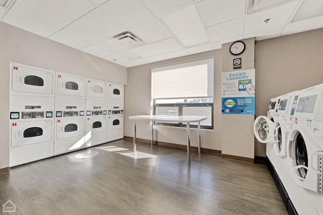 community laundry room with stacked washer and dryer, visible vents, washing machine and dryer, wood finished floors, and baseboards