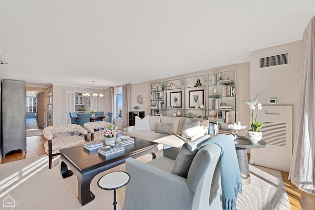 living area featuring an inviting chandelier, ornamental molding, light wood-style floors, and visible vents
