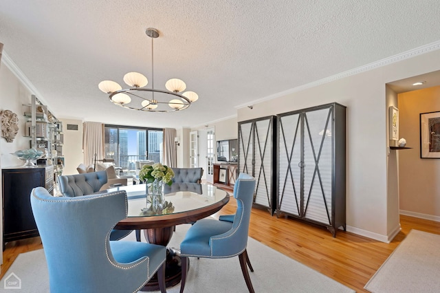 dining space featuring ornamental molding, light wood finished floors, a textured ceiling, and a notable chandelier