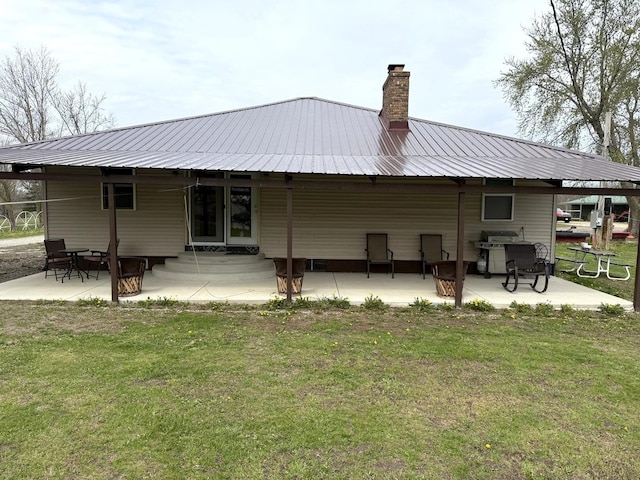 back of house featuring a yard, a chimney, metal roof, and a patio area