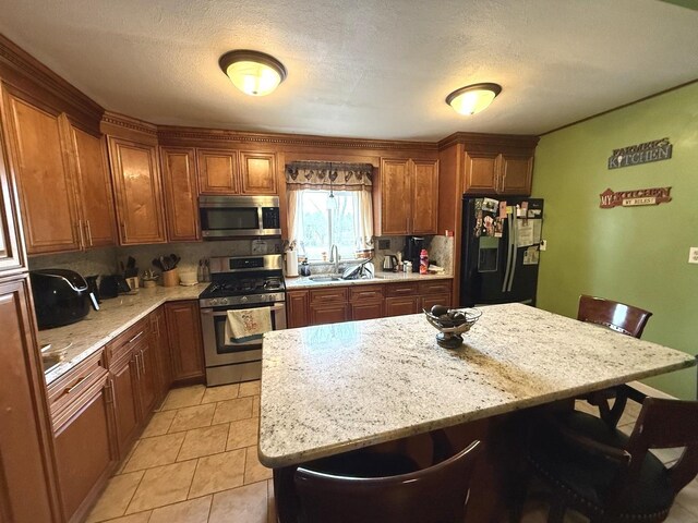 kitchen with brown cabinetry, light stone countertops, a sink, a breakfast bar, and stainless steel appliances