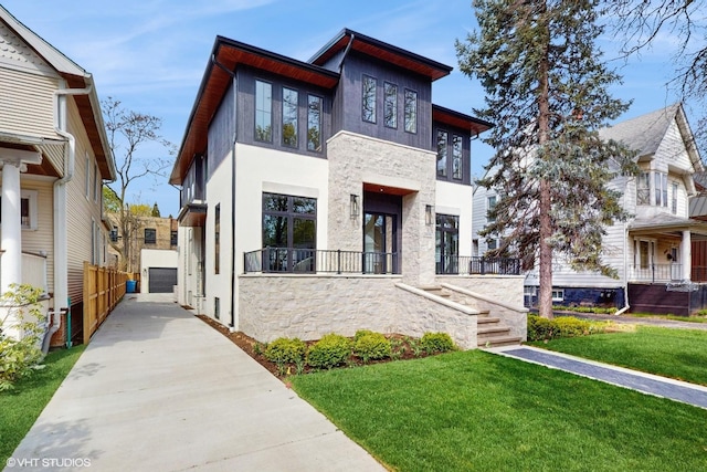 contemporary house with a detached garage, a front lawn, stone siding, and stucco siding