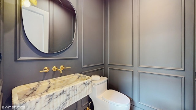 half bathroom featuring vanity, toilet, and a decorative wall
