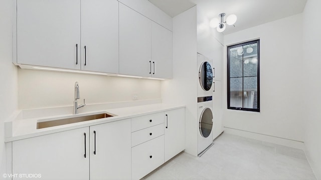 laundry area featuring light tile patterned floors, stacked washer and clothes dryer, cabinet space, and a sink