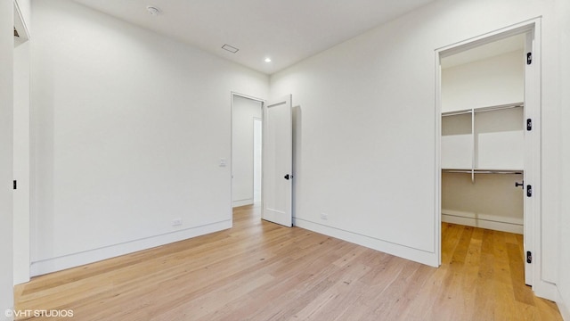 unfurnished bedroom featuring wood finished floors, a spacious closet, recessed lighting, and baseboards