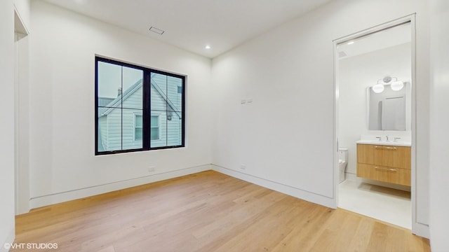 unfurnished bedroom featuring light wood-style flooring, a sink, baseboards, recessed lighting, and ensuite bath