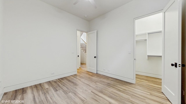 unfurnished bedroom featuring a spacious closet, baseboards, light wood finished floors, and a closet