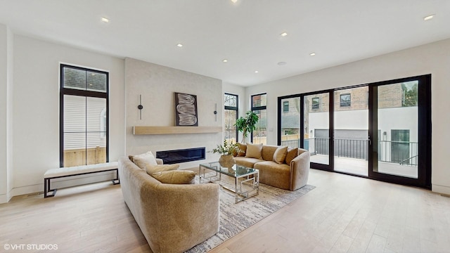 living area featuring baseboards, recessed lighting, light wood-style flooring, and a glass covered fireplace
