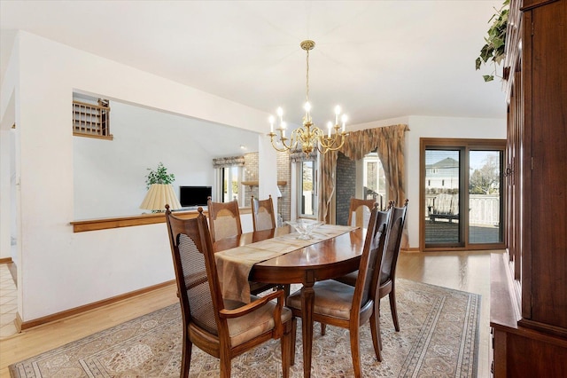 dining room with baseboards, a notable chandelier, lofted ceiling, and light wood finished floors