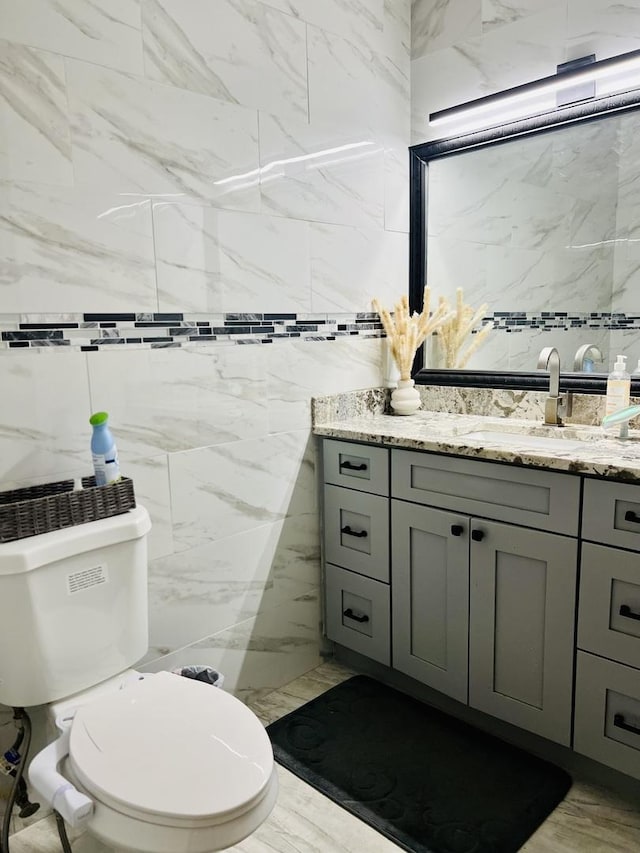 bathroom with toilet, vanity, and tile walls