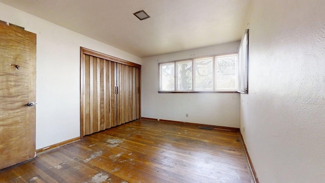 unfurnished bedroom featuring wood-type flooring, baseboards, and a closet