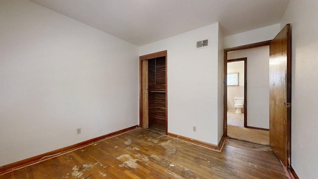 unfurnished bedroom featuring baseboards, a closet, hardwood / wood-style flooring, and visible vents