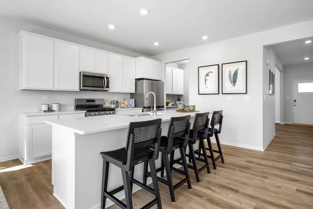 kitchen featuring light wood finished floors, stainless steel appliances, a kitchen island with sink, baseboards, and light countertops