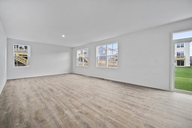 unfurnished living room featuring wood finished floors, a wealth of natural light, and baseboards