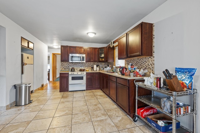 kitchen with tasteful backsplash, white appliances, glass insert cabinets, light countertops, and light tile patterned flooring