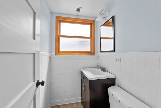 half bathroom with wainscoting, vanity, toilet, tile walls, and visible vents