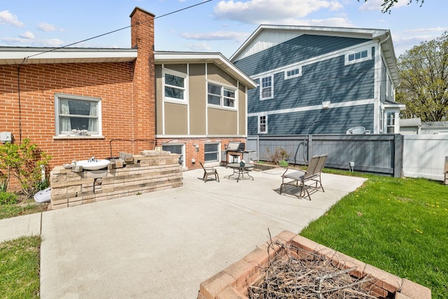 back of property featuring a chimney, a lawn, a patio area, brick siding, and fence