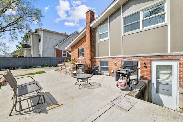 rear view of house with fence, stucco siding, a chimney, brick siding, and a patio area