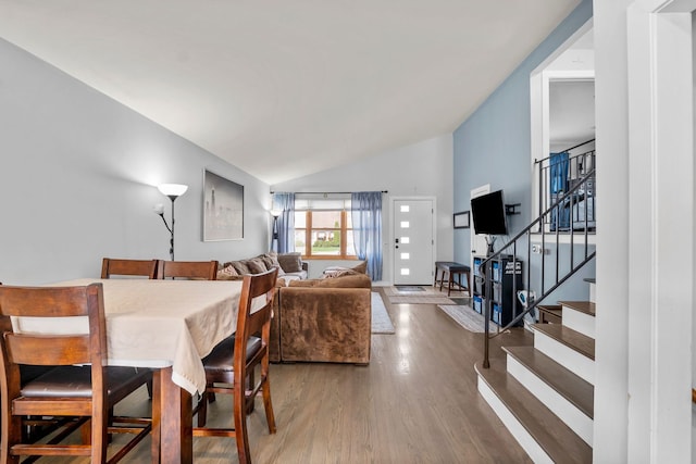 dining area featuring wood finished floors, vaulted ceiling, and stairway