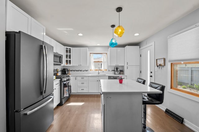 kitchen featuring a sink, stainless steel appliances, light wood-type flooring, visible vents, and a kitchen bar