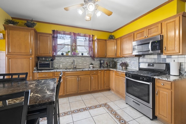 kitchen with a sink, stainless steel appliances, light tile patterned floors, stone counters, and a ceiling fan